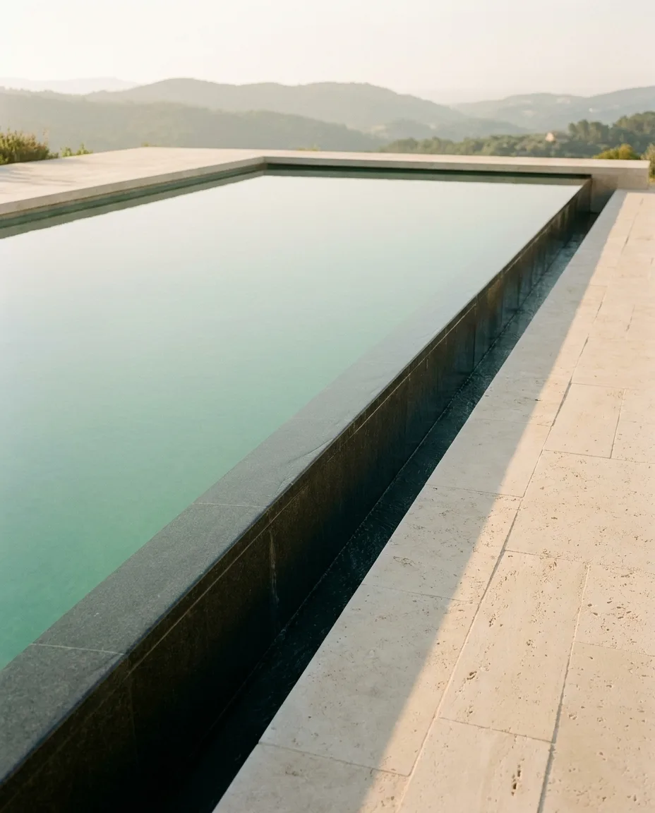 A minimalist vanishing-edge pool with travertine coping at golden hour